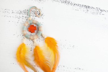 Parlak çok renkli Rüya yakalayıcı turuncu bir haç ve beyaz eski püskü ahşap zemin üzerinde turuncu sarı tüyleri ile. Metin için yer kopyalayın.