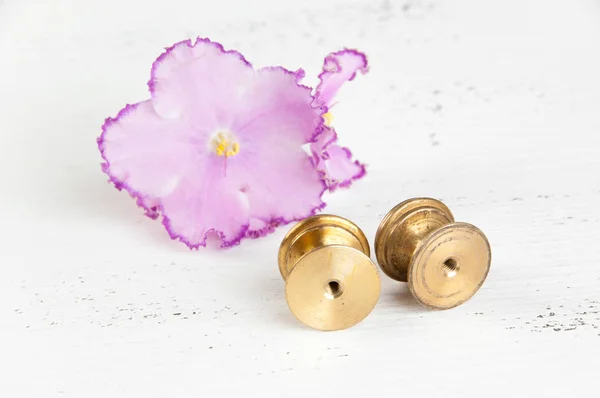 Two vintage bronze drawer pull knobs and flower violet on shabby white wooden background. Copy space for text.