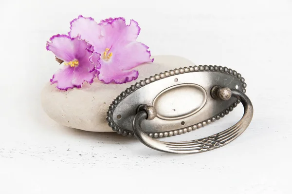 Vintage metal drawer pull knob and flowers violet on shabby white wooden background. Copy space for text.