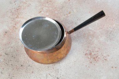 Beton arka planda kapağı ve siyah sapı olan klasik bakır güveç. Metin için alanı kopyala