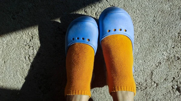 women\'s feet in blue sandals and orange socks in the sun