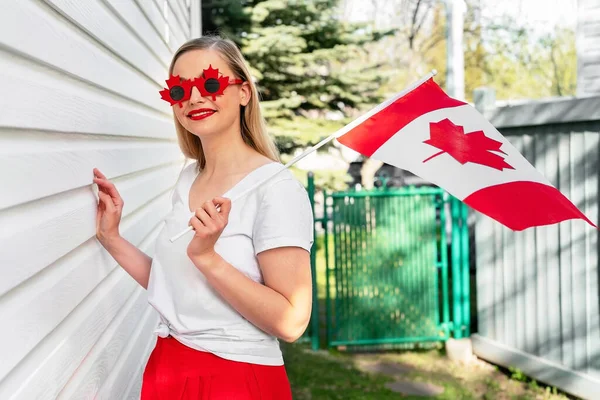 Happy Canada Day concept. Woman with Canadian flag smiling wearing fancy sunglasses looking to the camera. Proud Canadian.