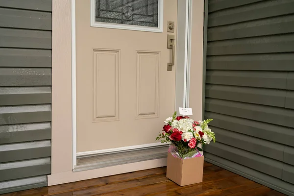 在房子门阶上的一个纸盒里有一束红色的白色花。令人惊讶的非接触式送花. 图库图片