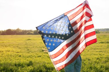 Gün batımında parktaki sahada Amerikan bayrağı taşıyan bir kadın. Arka plan.