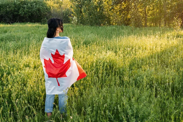 快乐加拿大日庆祝的概念。布鲁内特的女人背对着加拿大国旗，背对着自然背景。背景色. 图库图片