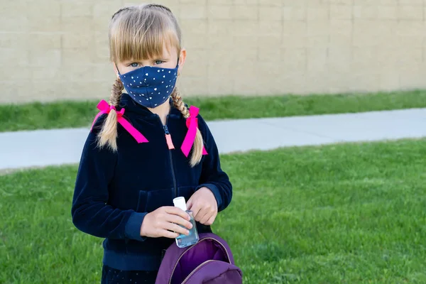 年轻的学生带着防护棉面罩上学，拿着手部清洁剂。回到学校，重新开始, 图库图片