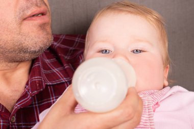 Baba kızını biberondan besliyor, yakın plan.