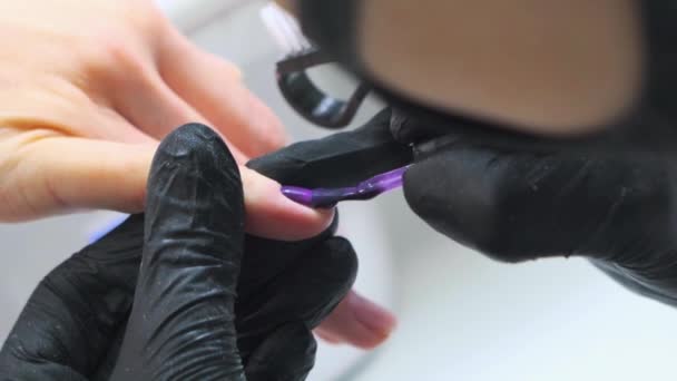 Художник ногтей покрывает ногти фиолетовым лаком — стоковое видео