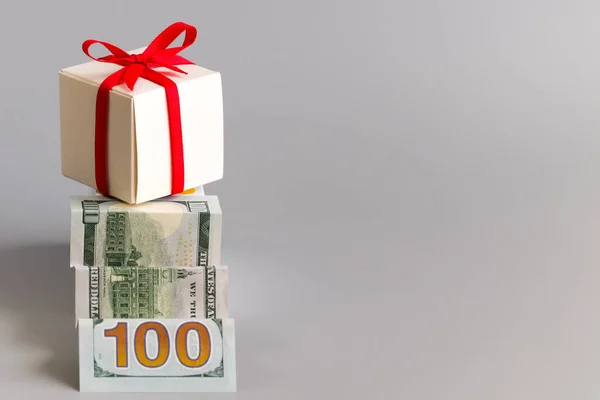 Bir merdiven gibi katlanmış yüz dolar ve kırmızı kurdeleyle bağlanmış bir hediye kutusu. İstifçilik, zenginlik ve sürpriz kavramı. Metin için boş alan