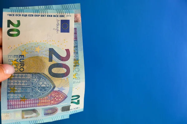 Bir kadının elinde parlak mavi bir arka planda yirmi avroluk banknotlar var. Nakit para konsepti, veresiye para, nakit ödeme..