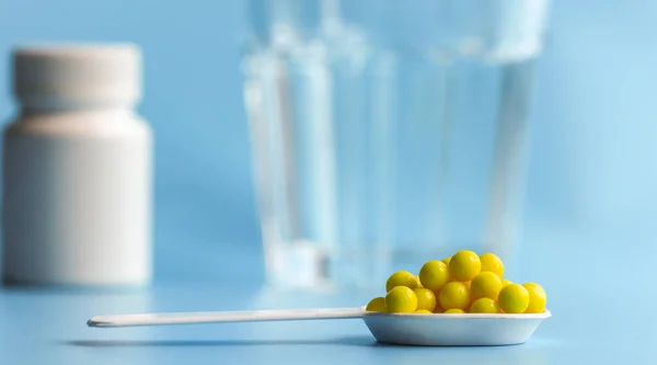 Cam bir bardağın arka planında beyaz bir kaşık içinde su ve beyaz ilaç şişesiyle vitamin ya da ilaç hapları. Gıda katkı maddesi, tıbbi ürün, sağlık kavramı.