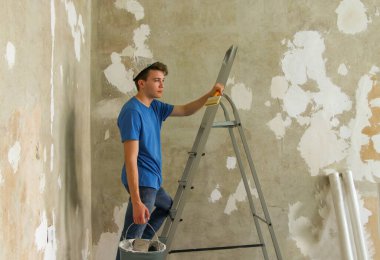 Ev yapımı gazete şapkalı genç bir adam, elinde bir inşaat kovası, bir merdivene tırmandı. Dairenin tamiri konsepti