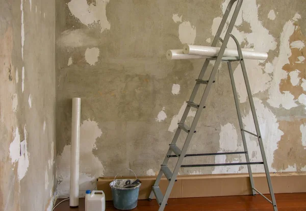 Aluminum stepladder, construction bucket and rolls of Wallpaper on the background of a plastered wall. Concept of renovation in the apartment