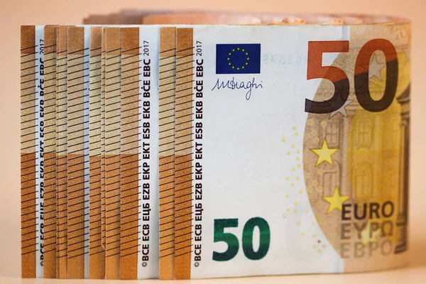 Paper money with a face value of 50 euros, folded in half, is arranged in a row on a light background. Close up.