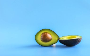 Taze avokado meyvesi ikiye bölünmüş. Olgun, tereyağlı avokado eti ve mavi arka planda bir taş. Kopyalamak için boş yer. Yaratıcı yaz yemekleri konsepti.