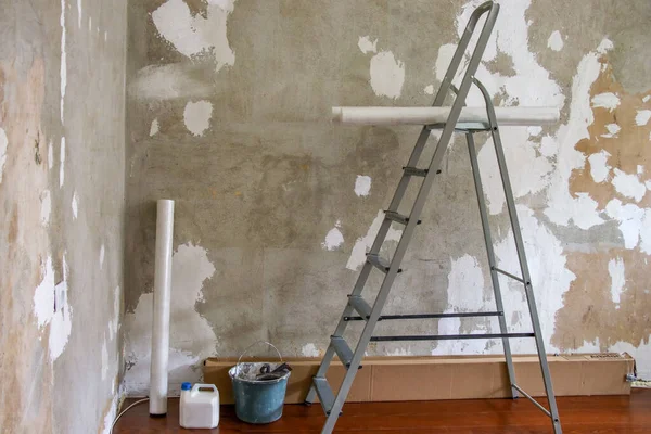 Aluminum stepladder, construction bucket and rolls of Wallpaper on the background of a plastered wall. Concept of renovation in the apartment