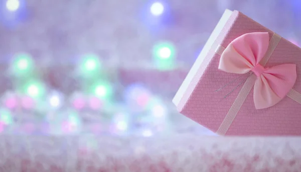 Caja de regalo de Navidad de color rosa suave sobre un fondo desenfocado con luces ardientes de una guirnalda. Fondo de Navidad. Espacio libre para copiar. — Foto de Stock