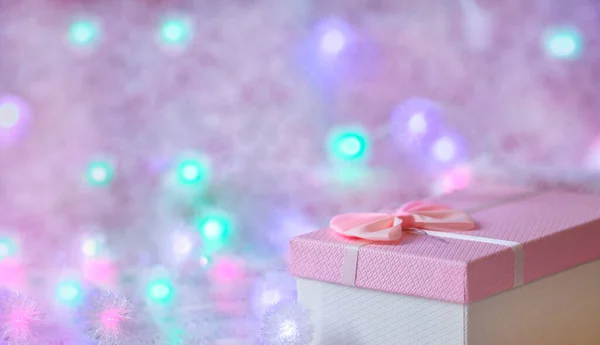 Une boîte cadeau de couleur rose tendre sur un fond déconcentré avec des lumières brûlantes d'une guirlande. Festive, fond de Noël. Espace libre pour copier. — Photo