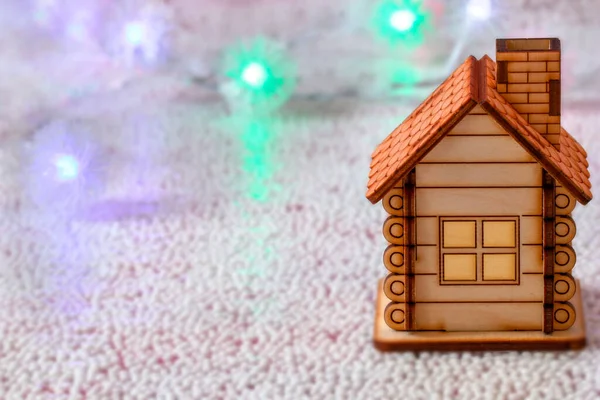 Houten speelgoedhuis op een onscherpe achtergrond met bloemenslingers van licht. Het concept van een familievakantie. Feestelijke kerstachtergrond. Vrije ruimte om te kopiëren. — Stockfoto
