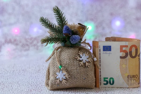 Noel hediyesi çantası ve 50 Avro 'luk banknot. Odaklanmamış arka plan ve ışık çelenkleri. Noel ve yeni yıl tatilleri için hediyeler ve sürprizler konsepti. Noel satışları ve indirimler.
