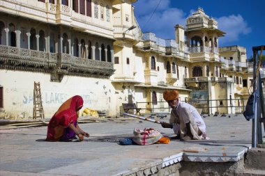 Udaipur, Hindistan - 22 Mayıs 2013: Hint geleneksel giysileri içinde bir Rajasthani erkek ve kadın Bagore Ki Haveli gölünün arkasında Pichola Gölü kenarında oturuyor