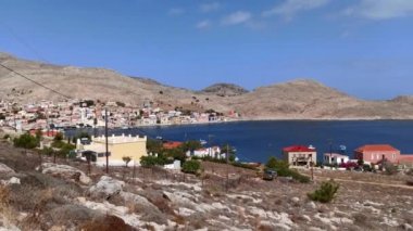 Rodos - Yunanistan: Kristal berrak mavi deniz suyundaki paslı kayalık tepelere karşı yazın Halki (Chalki) Adası 'nda beyaz evleri olan kentin Pan çekimi