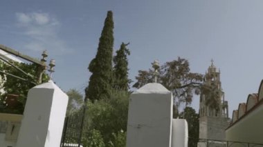 Suriye Adası, Yunanistan - 25 Eylül 2020: Akdeniz kıyısındaki limanının yanındaki ortaçağ kilisesinin yanındaki yeşil bitkilerle kaplı evler. Sınıflandırılmamış / düz çalışma profili.
