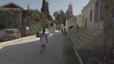 Symi, Yunanistan - 25 Eylül 2020: Akdeniz kıyısındaki liman yakınlarında ortaçağ kilisesi yakınlarındaki bir adada yürüyen genç bir kız. Sınıflandırılmamış / düz çalışma profili
