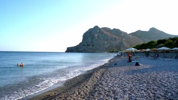 ギリシャのロードス島 2020年9月25日 地中海の島に位置する背景に岩の多い山に対して ロープのビーチを冷却し 楽しむ人々 — ストック動画