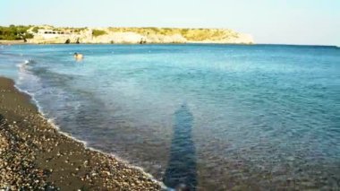 Rodos, Yunanistan: 25 Eylül 2020: Akdeniz adasının arka planında yer alan kayalık dağa karşı batan, yüzen ve güneşin tadını çıkaran insanlar