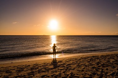 Gün batımında sahilde yürüyen bir kadının silüeti.