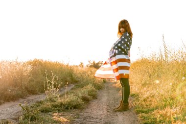 Birleşik Devletler bayrağıyla heyecanlı genç bir kadın doğada günbatımının tadını çıkarıyor. ABD 'nin 4 Temmuz bağımsızlık günü