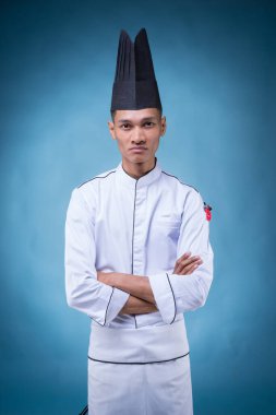 Beyaz üniformalı, önlüklü ve mavi şapkalı Asyalı bir yönetici şefin portresi.