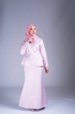 Geleneksel elbise ve tesettüre bürünmüş güzel bir kadın modelin tam boy portresi, gri arka planda yaşayan Müslüman kadınlar için bir yaşam tarzı. Idul Fitri ve tesettür moda konsepti.