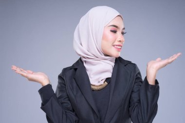 Çekici bir Müslüman iş kadınının yarım boy portresi karışık pozlar ve gri arka planda izole edilmiş jestlerle tesettüre girmiş. Şirket, teknoloji, iş ya da finans için görüntü kesimi.