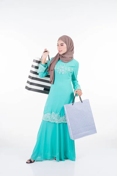 一位美丽而兴奋的穆斯林女模特穿着亚洲传统服饰 穿着时髦的和服 背着白色背景的购物袋 Eidul Fitri节庆准备购物概念 全长肖像 — 图库照片