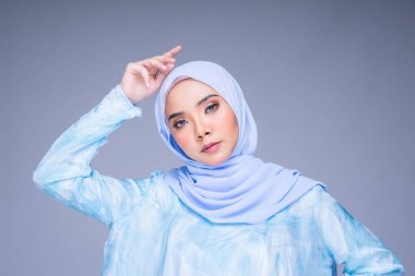 Geleneksel elbise ve tesettüre bürünmüş güzel bir kadın modelin portresi. Gri arka planda izole edilmiş Müslüman kadınlar için bir yaşam tarzı. Idul Fitri ve tesettür moda konsepti.