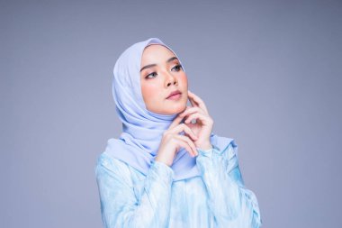 Geleneksel elbise ve tesettüre bürünmüş güzel bir kadın modelin portresi. Gri arka planda izole edilmiş Müslüman kadınlar için bir yaşam tarzı. Idul Fitri ve tesettür moda konsepti.