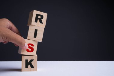 Mali risk değerlendirmesi, risk ödülü ve portföy risk yönetimi konsepti. Küplere R, I, S, K harfleri dizilmiş dört tahta küp. Bir küpü hareket ettirmeye çalışan bir el. Boşluğu kopyala.