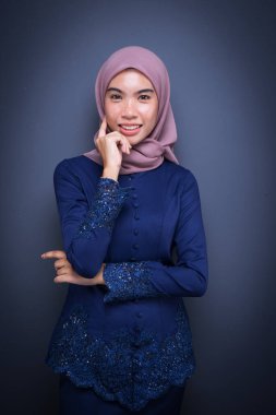 Koyu mavi, tesettürlü bir modern kebaya giyen güzel bir Müslüman kadın model. Gri arka planda izole edilmiş Asyalı Müslüman geleneksel bir elbise. Eidul Fitri moda ve yaşam tarzı portresi konsepti.