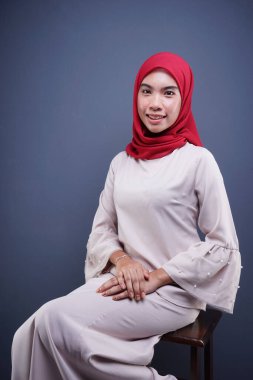 Gri arka planda izole edilmiş Asyalı Müslüman geleneksel bir elbise olan kırmızı tesettürlü, krem renkli modern kebaya giymiş güzel bir Müslüman kadın modelin yakın çekimi. Eidul Fitri moda ve yaşam tarzı portresi konsepti.
