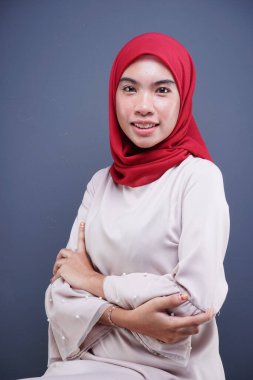 Gri arka planda izole edilmiş Asyalı Müslüman geleneksel bir elbise olan kırmızı tesettürlü, krem renkli modern kebaya giymiş güzel bir Müslüman kadın modelin yakın çekimi. Eidul Fitri moda ve yaşam tarzı portresi konsepti.