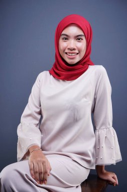 Gri arka planda izole edilmiş Asyalı Müslüman geleneksel bir elbise olan kırmızı tesettürlü, krem renkli modern kebaya giymiş güzel bir Müslüman kadın modelin yakın çekimi. Eidul Fitri moda ve yaşam tarzı portresi konsepti.