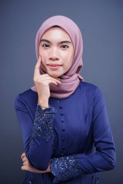 Koyu mavi, tesettürlü bir modern kebaya giyen güzel bir Müslüman kadın model. Gri arka planda izole edilmiş Asyalı Müslüman geleneksel bir elbise. Eidul Fitri moda ve yaşam tarzı portresi konsepti.