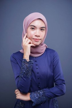 Koyu mavi, tesettürlü bir modern kebaya giyen güzel bir Müslüman kadın model. Gri arka planda izole edilmiş Asyalı Müslüman geleneksel bir elbise. Eidul Fitri moda ve yaşam tarzı portresi konsepti.
