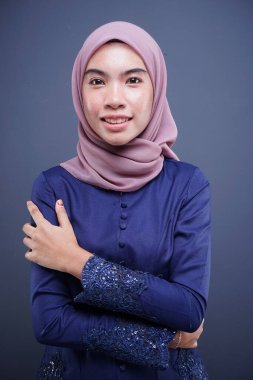 Koyu mavi, tesettürlü bir modern kebaya giyen güzel bir Müslüman kadın model. Gri arka planda izole edilmiş Asyalı Müslüman geleneksel bir elbise. Eidul Fitri moda ve yaşam tarzı portresi konsepti.