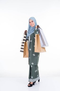 Geleneksel Asya elbisesi içinde güzel ve heyecanlı bir Müslüman kadın model beyaz arka planda izole edilmiş alışveriş torbaları taşıyor. Eidul Fitri moda ve festival hazırlık alışveriş konsepti
