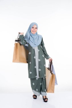 Geleneksel Asya elbisesi içinde güzel ve heyecanlı bir Müslüman kadın model beyaz arka planda izole edilmiş alışveriş torbaları taşıyor. Eidul Fitri moda ve festival hazırlık alışveriş konsepti