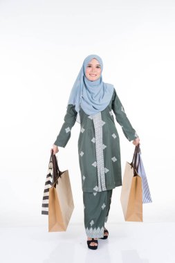 Geleneksel Asya elbisesi içinde güzel ve heyecanlı bir Müslüman kadın model beyaz arka planda izole edilmiş alışveriş torbaları taşıyor. Eidul Fitri moda ve festival hazırlık alışveriş konsepti