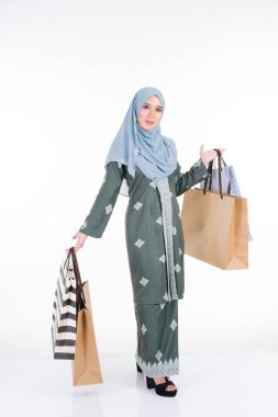 Geleneksel Asya elbisesi içinde güzel ve heyecanlı bir Müslüman kadın model beyaz arka planda izole edilmiş alışveriş torbaları taşıyor. Eidul Fitri moda ve festival hazırlık alışveriş konsepti
